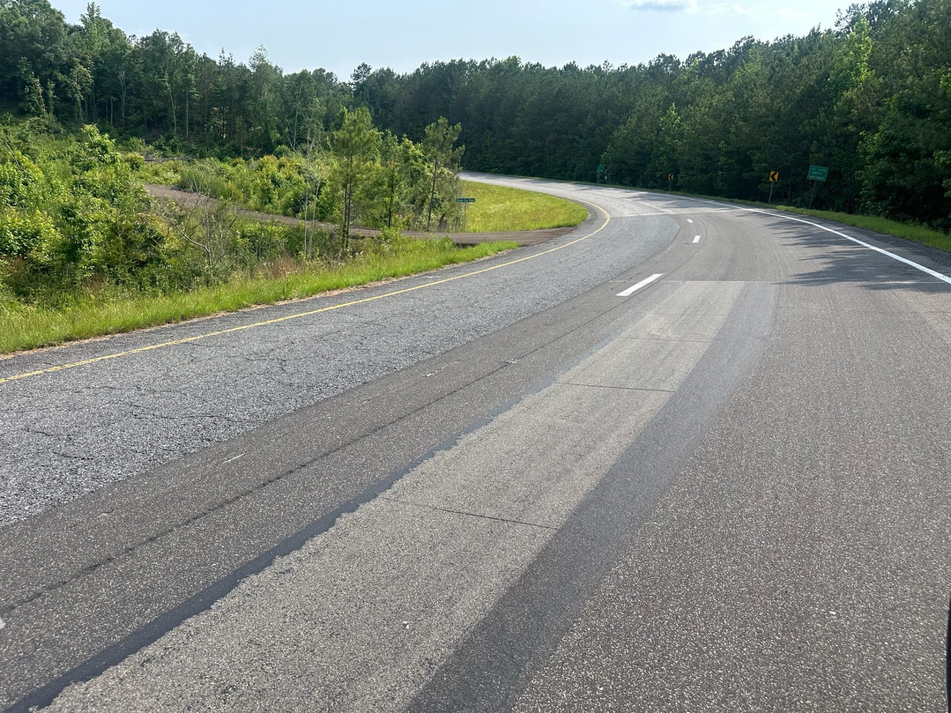 A light-gray Roadway Safety Strip test strip installed in the traffic lane of a curved, tree-lined roadway