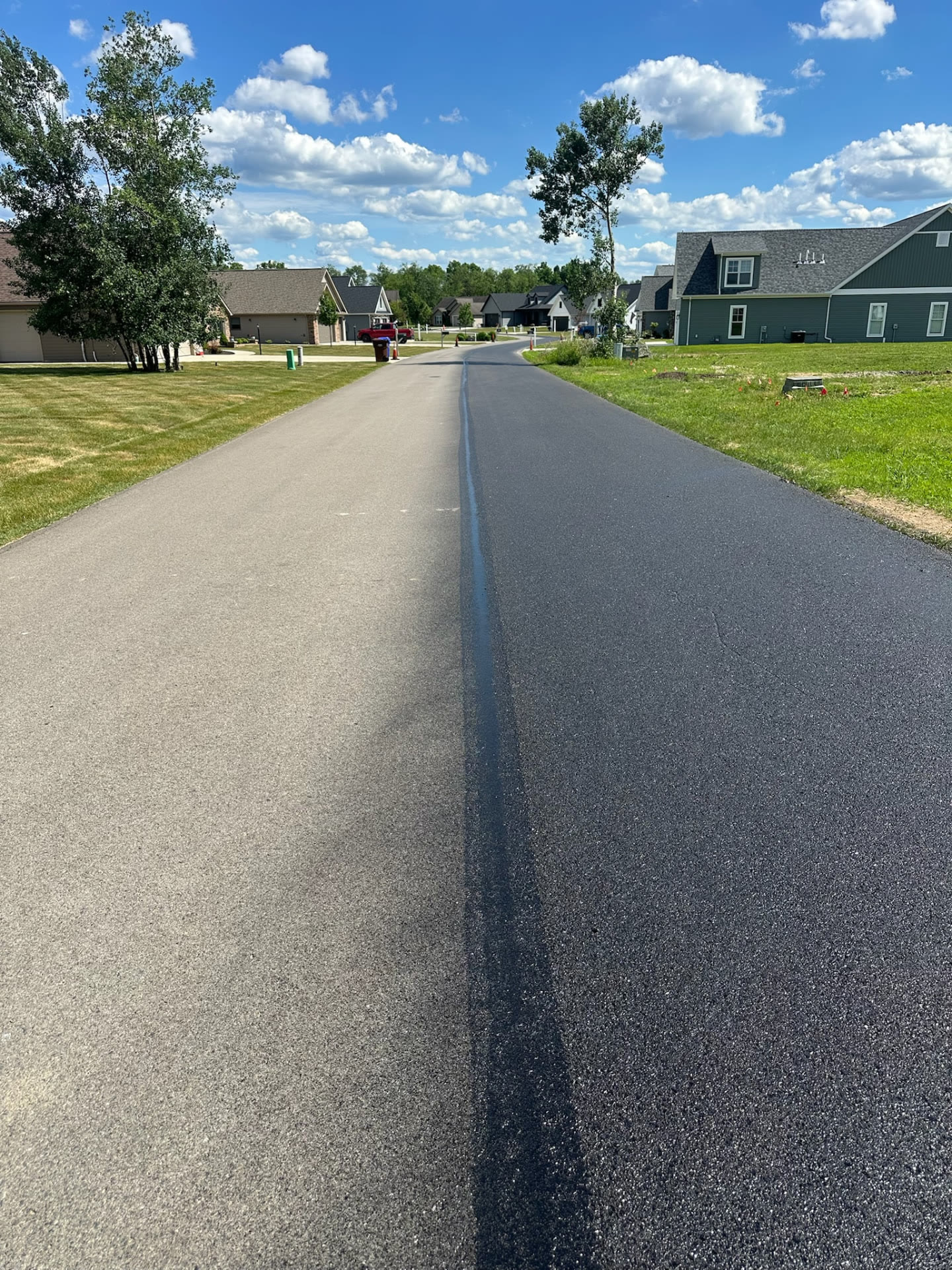Residential street showing a clear vertical split between untreated faded pavement on the left and dark RevivaRoad-treated pavement on the right